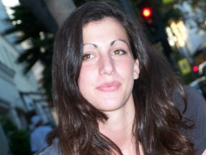 A brunette in a short skirt poses on white sheets. Thumbnail 1